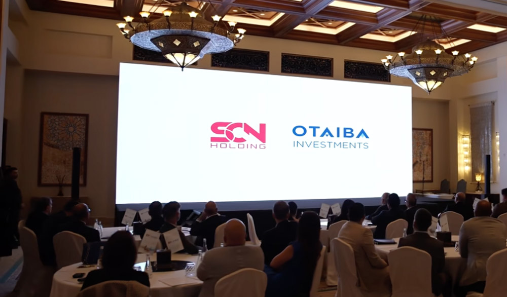 Screen in a ballroom with the SCN Holding and Otaiba Investments logos